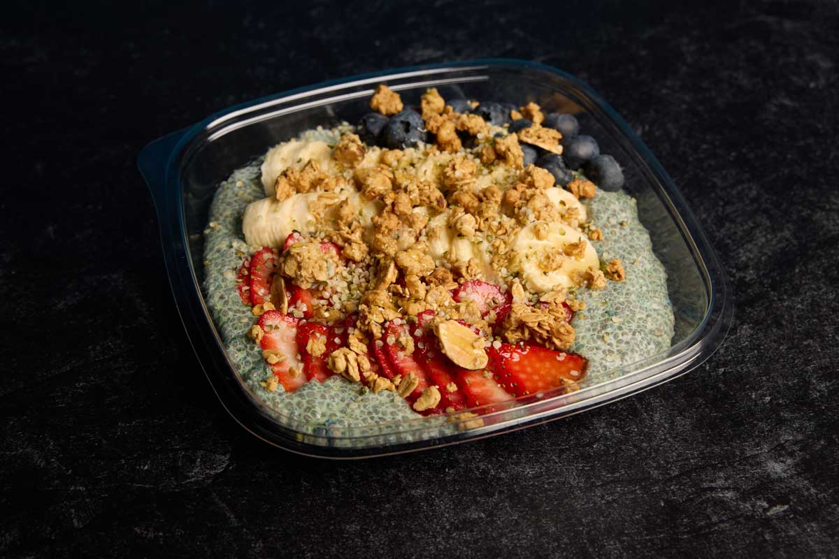 Blue spirulina chai smoothie bowl with sliced fresh strawberries, bananas, and blueberries, topped with hemp seeds, and granola.