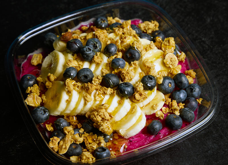 hot pink dragon fruit smoothie bowl with sliced bananas, blueberries, and granola