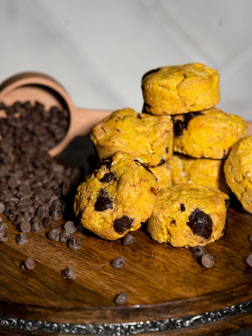 Stack of 8 pumpkin colored cookie bites with chocolate chips that are next to a mound of chocolate chips.