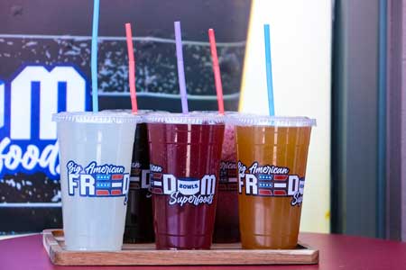 Healthy fresh red, orange, and white juice in clear cups that say Big American Freedom Bowls Superfoods.